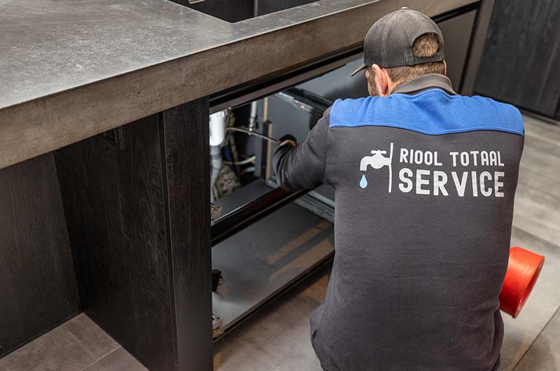 Monteur van Riool Totaal Service werkt aan de afvoer onder een keukenblok