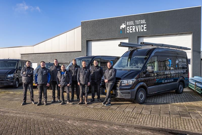 Het team van Riool Totaal Service voor het pand, met de zwarte bedrijfsbussen